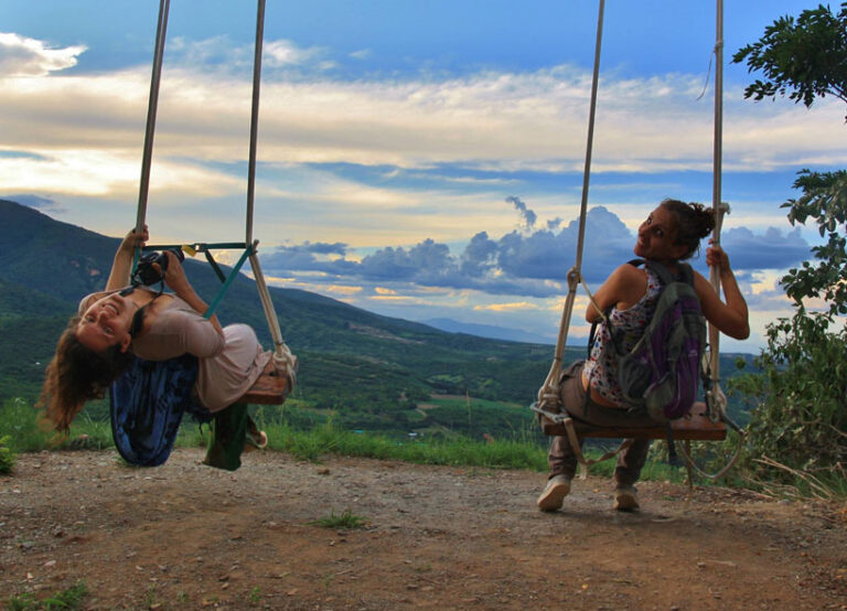 two people on swings, with a view on a green valley