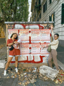 Two people standing in front of the posters they laid out, gesturing to the posters and smiling